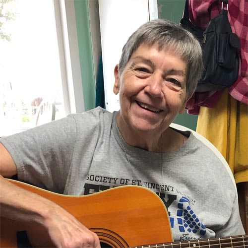 Sara, one of RedwoodESL's tutors, smiling at the camera while holding a guitar